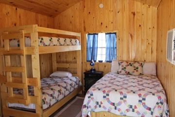 Pictured is the interior of our Cozy Cabins. Shown in the photo is the full size bed and twin bunk beds.