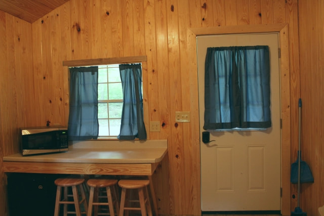 Pictured is the interior of our Cozy Cabins. Shown in the photo is the door way and the bar area. The bar has a microwave on top, three bar stools and a mini-fridge located underneath. 