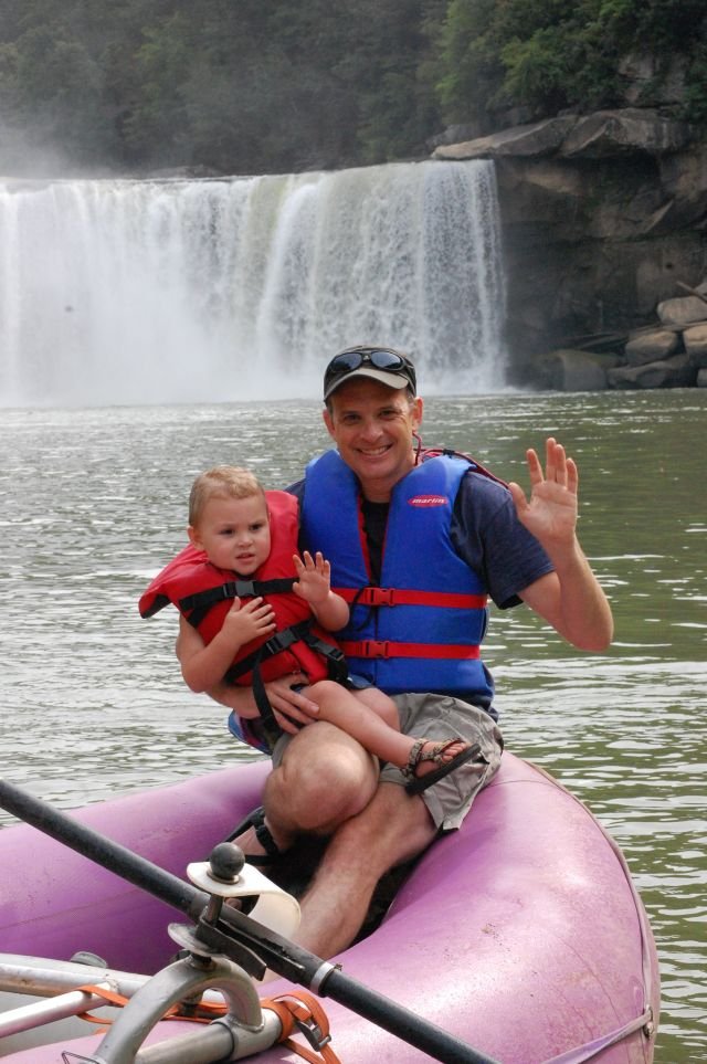 Man and baby on raft in front of falls