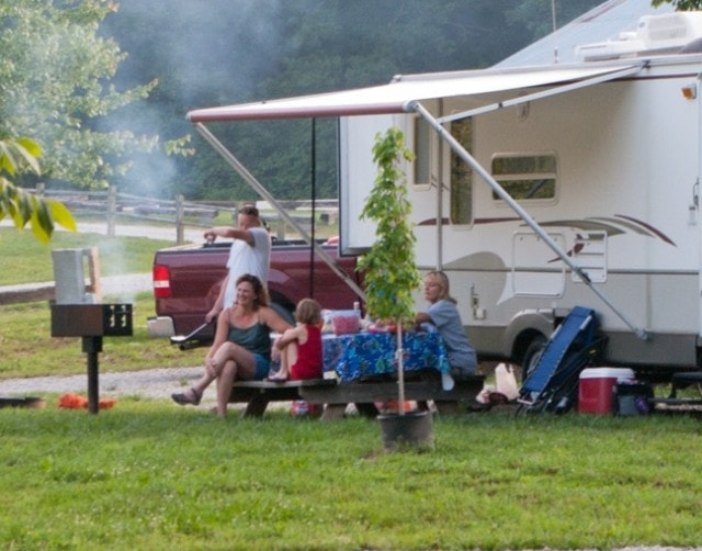 A family camping in one of our RV campsites through the summer season. They are pictured sitting at their picnic table waiting on their food to finish cooking on the grill. 