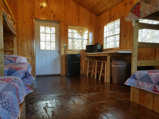 Pictured is our Super Cozy Cabin from the front doorway, looking in. This point of view allows us to see all of the bunks in the cabin partially. It also shows the bar and bar stools, microwave, mini-fridge, and back porch access. 